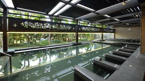 A modern indoor pool area with clear glass walls, a view of greenery outside, and a series of steps leading into the pool. - Spring Hill Resort (Kaohsiung)