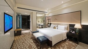A modern hotel room with a large bed, a bedside table with a lamp, a flat-screen TV, and a bench. - Rainbird International Hotel (Chengdu)