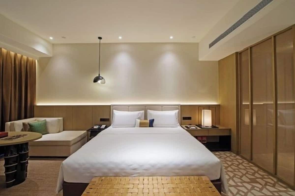 A modern hotel room with a large bed, bedside tables, a desk, and a seating area.