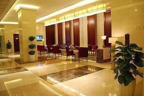 Un vestíbulo de hotel con mostrador de recepción, zona de estar y una planta grande.