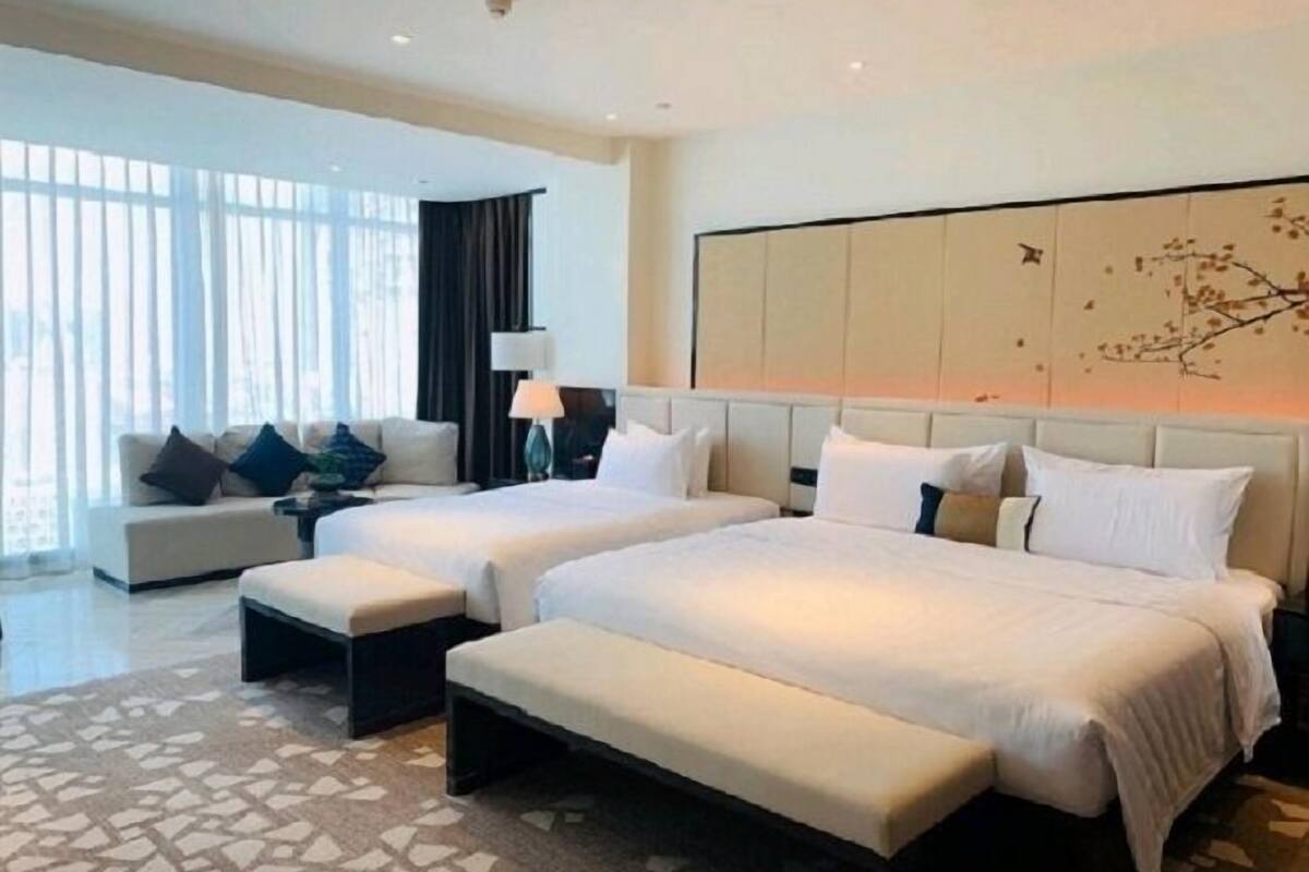 A hotel room with two beds, a sofa, and a large window with curtains.