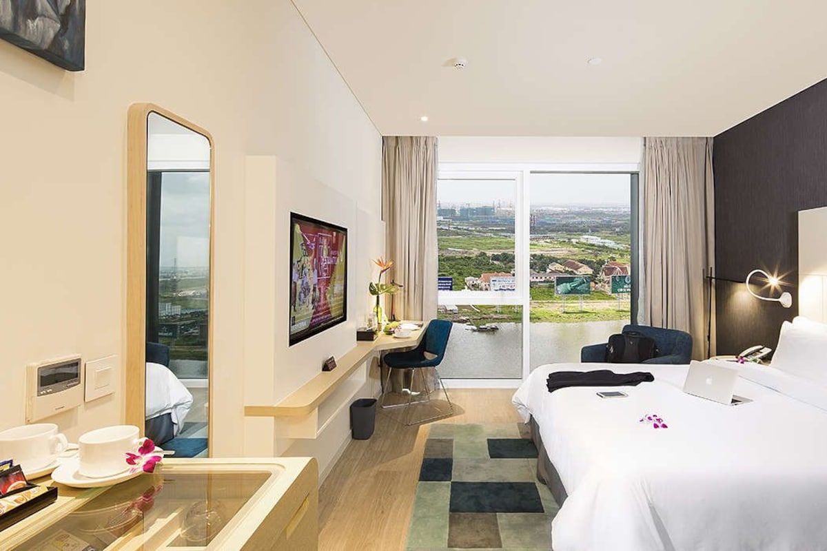 Habitación de hotel con cama, escritorio, silla y un amplio ventanal con vista a la ciudad.