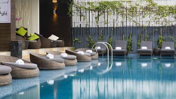 Uma área à beira da piscina com espreguiçadeiras e um pequeno espaço de estar com almofadas.