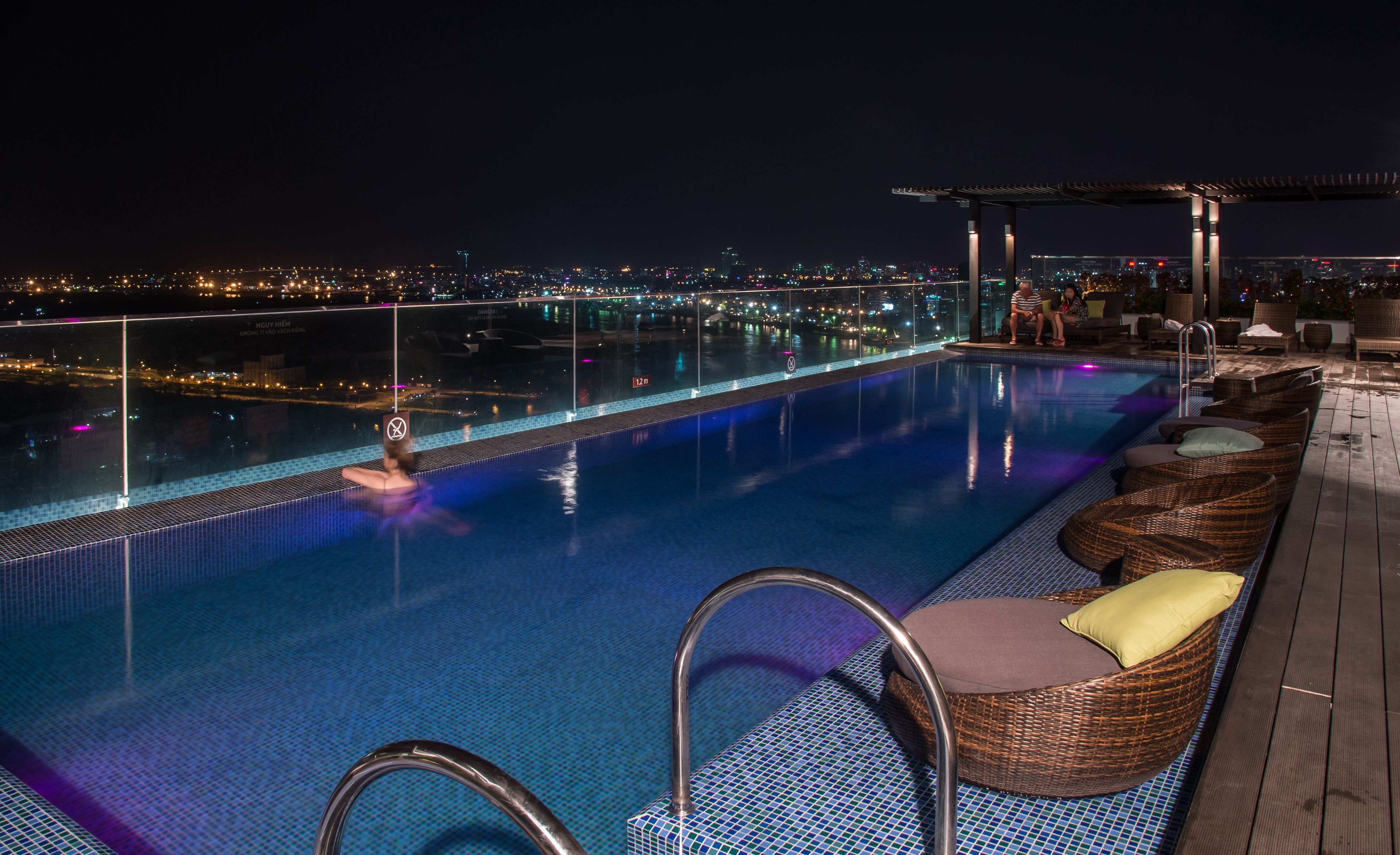 A rooftop infinity pool with a city view, lounge chairs, and a covered seating area.