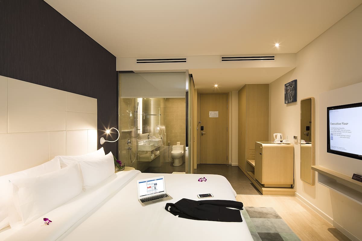 Quarto de hotel com uma cama, um laptop, um smartphone e um roupão sobre a cama.