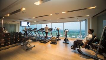 A modern gym with treadmills, weight machines, and a large TV screen.