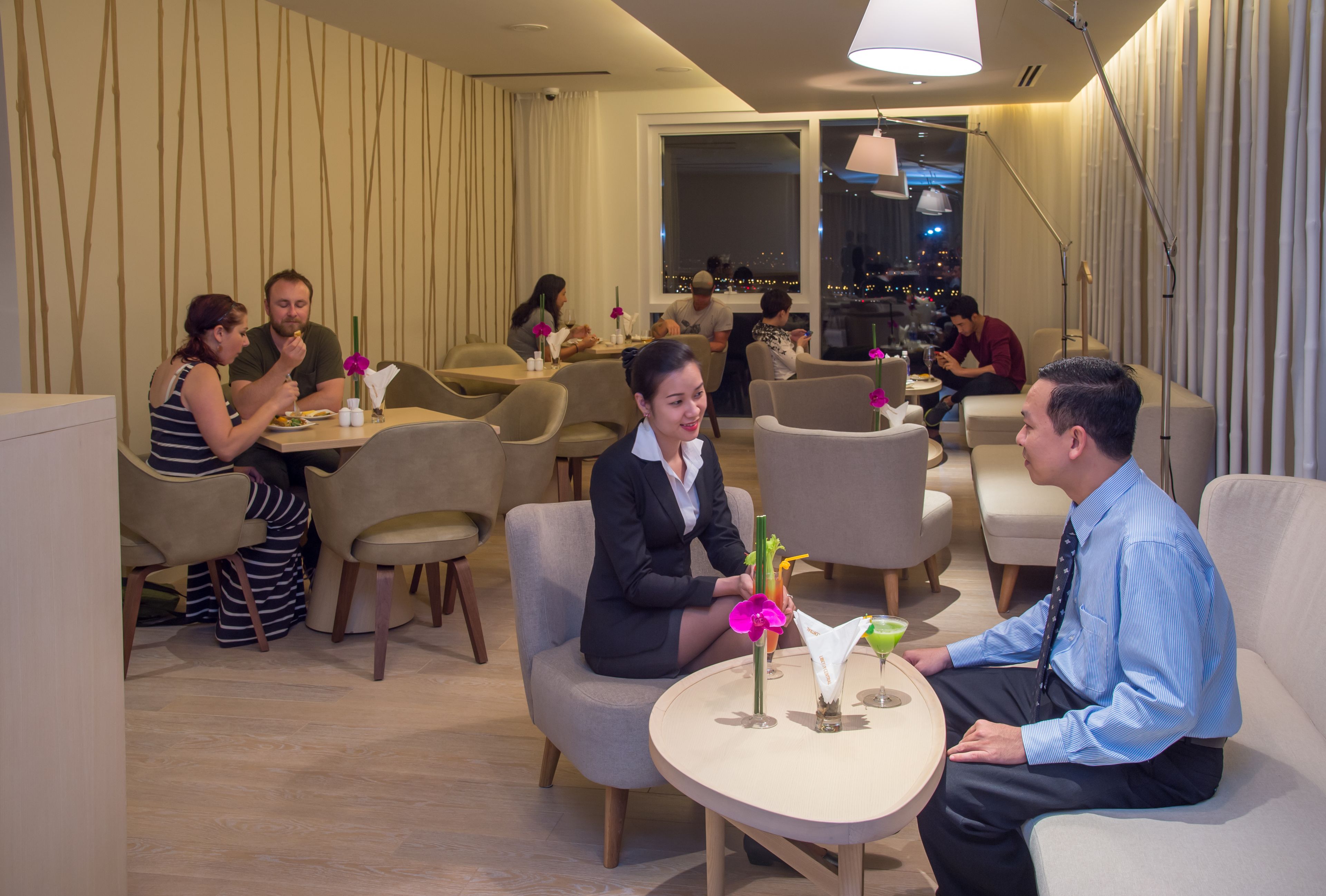 A modern hotel lobby with seating areas and a view of the cityscape through large windows.