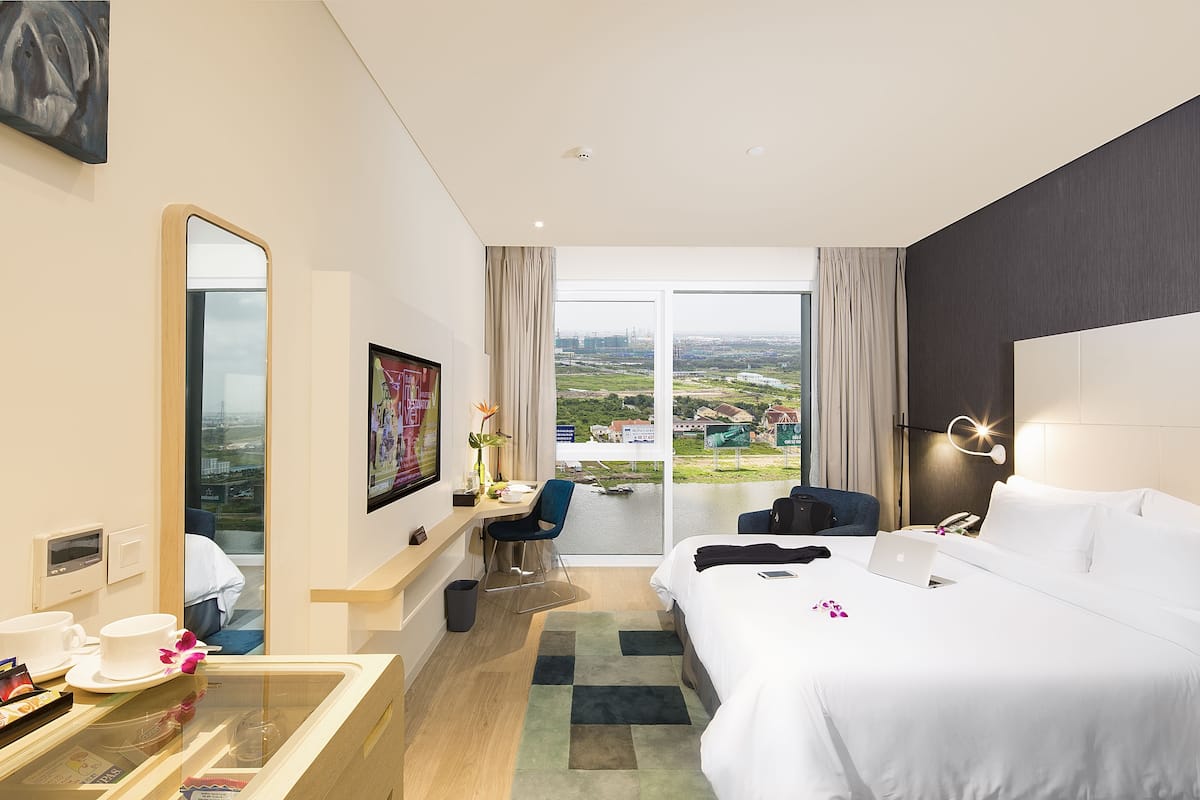 Quarto de hotel com cama, escrivaninha, cadeira e vista da cidade.