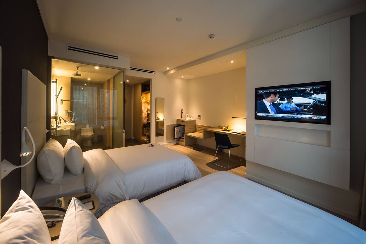 Quarto de hotel com duas camas, uma mesa, uma televisão e um banheiro.