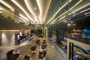 Een moderne hotel lobby met een receptiebalie, een zithoek en grote ramen met uitzicht op de straat.
