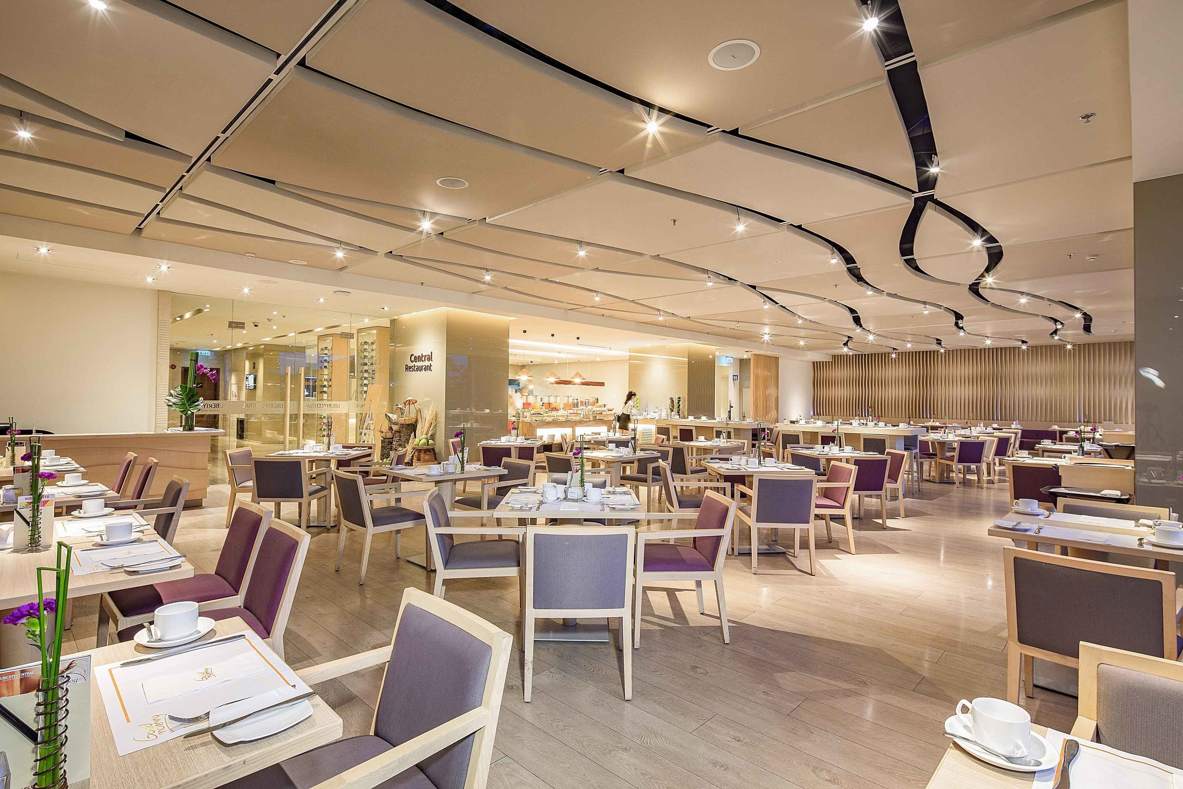 A spacious restaurant with multiple dining tables and chairs, a central counter, and a modern ceiling design.
