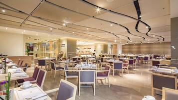 A spacious restaurant with multiple dining tables and chairs, a central counter, and a modern ceiling design.