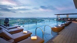 An infinity pool with lounge chairs and a glass railing overlooking a cityscape. - Liberty Central Saigon Riverside (Ho Chi Minh City)