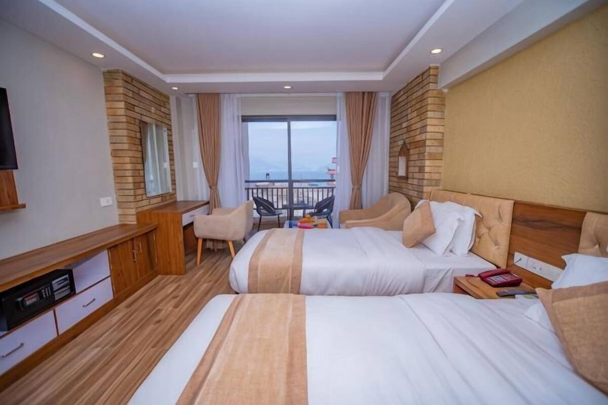 A hotel room with two beds, a desk, a TV, and a balcony with a view.