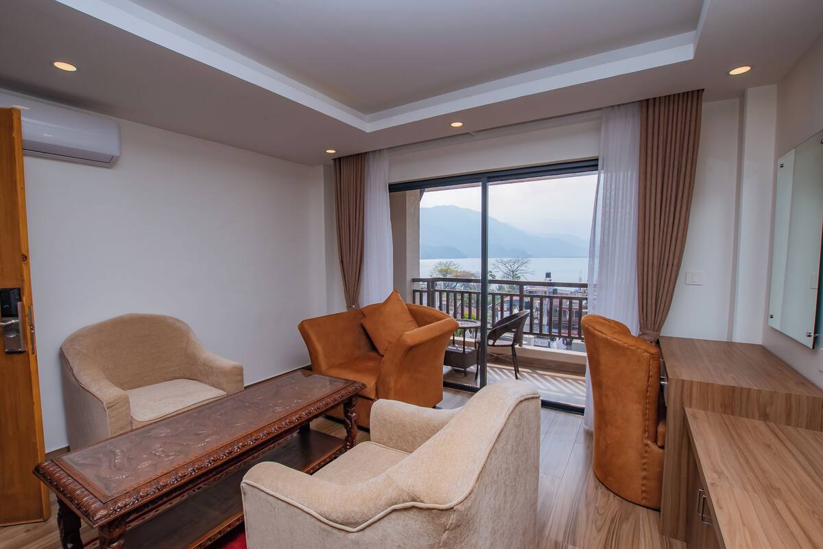 A hotel room with a sofa, armchairs, a wooden coffee table, and a balcony with a view of the mountains.