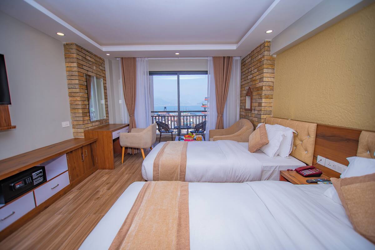 A hotel room with two beds, a TV, a desk, and a balcony with a view of the sea.