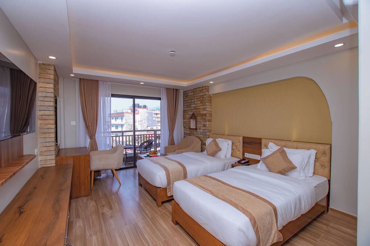 A hotel room with two beds, a wooden bench, a TV, and a balcony with a view of buildings.