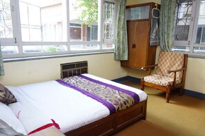 Une chambre à coucher avec un lit, une chaise en bois, une armoire et une fenêtre avec des rideaux.