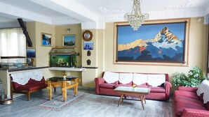 A living room with a red sofa, a wooden coffee table, a fish tank, and a painting of a mountain. - Hotel Blue Diamond (Kathmandu)