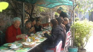Un groupe de personnes est réuni autour d’une table à l’extérieur, où elles dégustent divers plats et boissons.