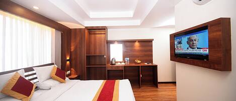 A hotel room with a large bed, a desk, a television, and an air conditioning unit.