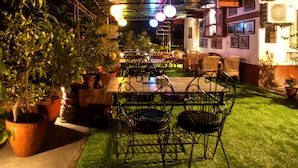 An outdoor patio area with a table and chairs, surrounded by potted plants and a grassy area. - Hotel Friend's Home (Kathmandu)