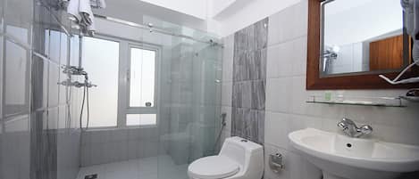 A modern bathroom with a glass-enclosed shower, a white toilet, and a sink with a mirror above it.