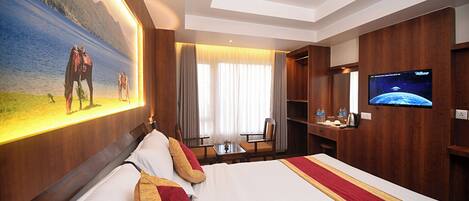A hotel room with a large bed, a desk, a chair, a television, and a painting of a scenic landscape.