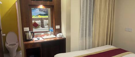 A hotel room with a bed, a desk with a telephone, a mirror, and a television.