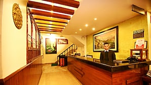 A hotel reception area with a wooden reception desk, a clock on the wall, and a framed picture above the desk. - Hotel Friend's Home (Kathmandu)