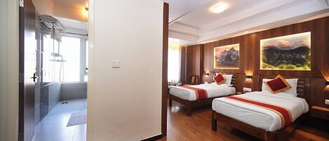 A hotel room with two beds, wooden flooring, a shower area, and wall-mounted artwork.