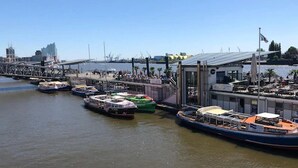 Un port de plaisance où sont amarrés plusieurs bateaux, un pont en arrière-plan et un bâtiment moderne doté d’une façade en verre.