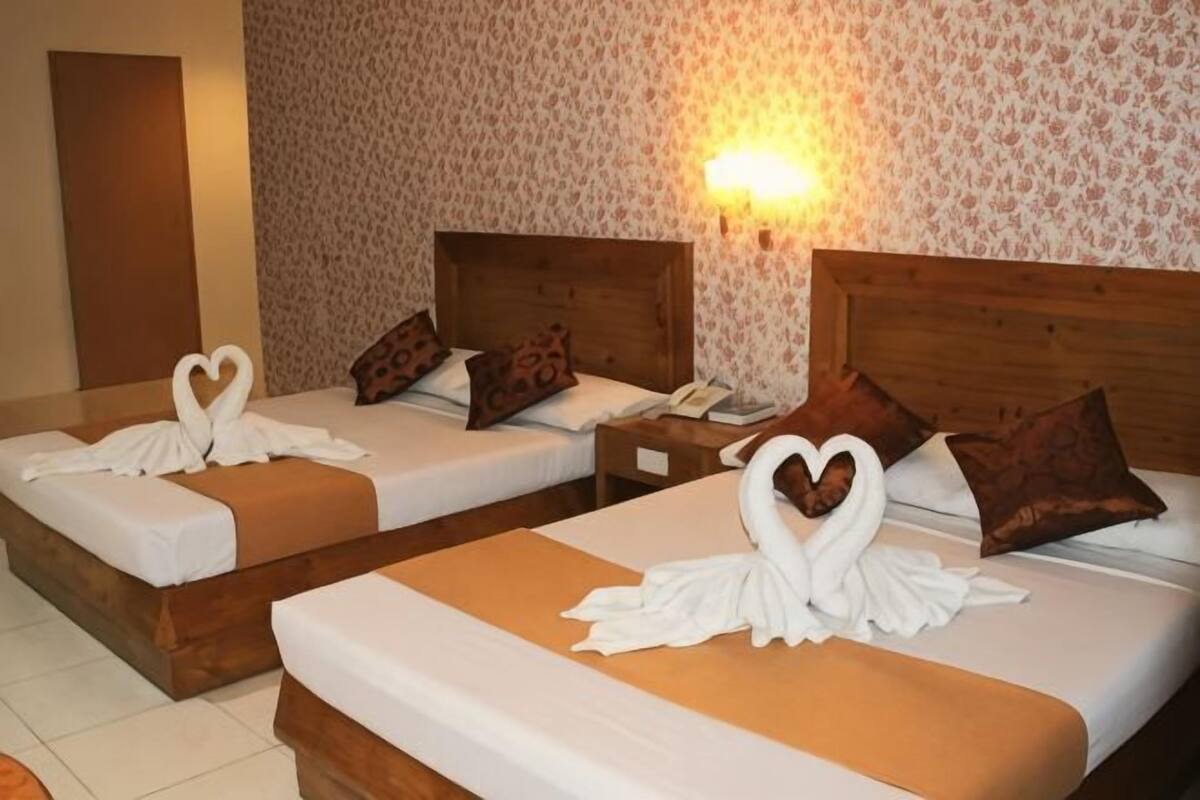 Two twin beds with heart-shaped towels, wooden headboards, and patterned wallpaper.