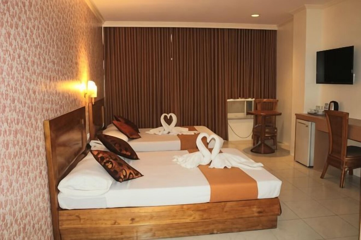 A hotel room with two beds, a desk, a chair, a television, and a wall-mounted TV.