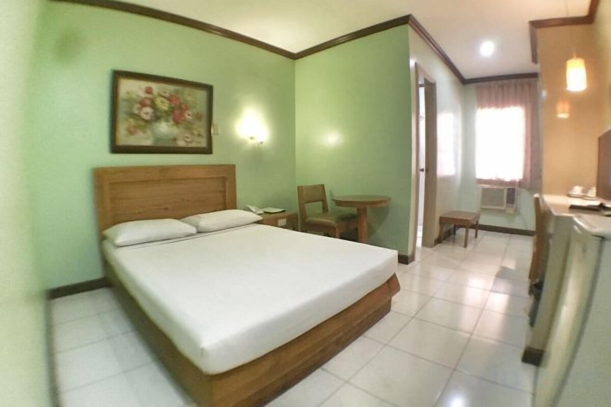 A hotel room with a bed, a chair, a small table, and a desk.