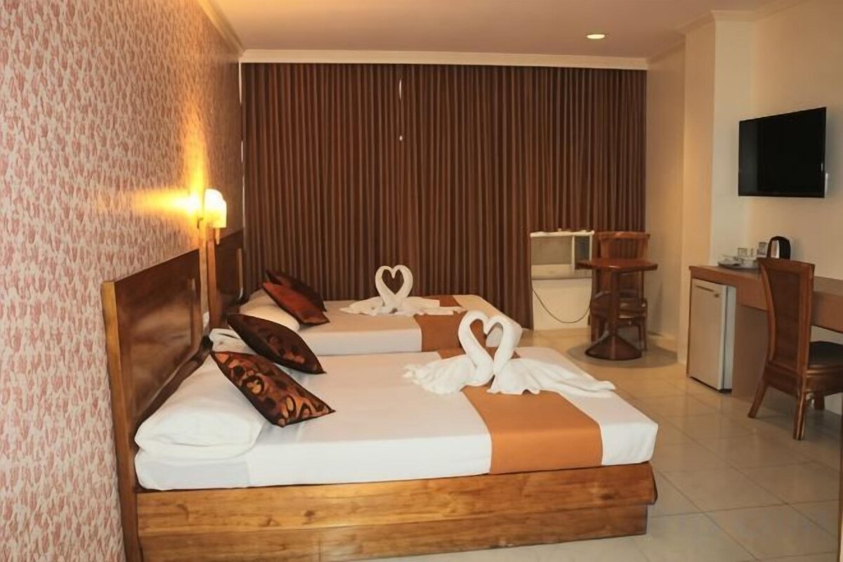 Une chambre d’hôtel avec deux lits, un bureau, une chaise, un téléviseur et un téléviseur fixé au mur.