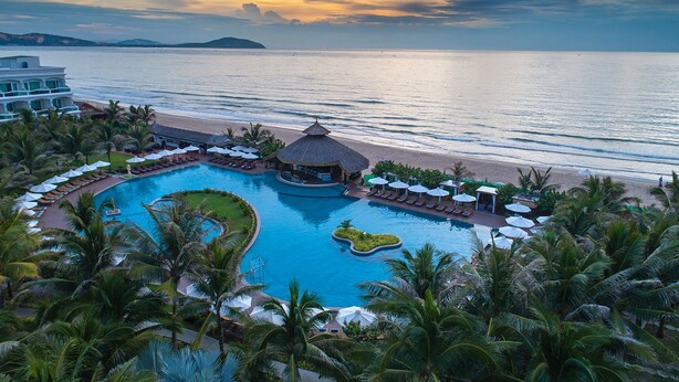 Un resort con piscina grande, acceso a la playa y palmeras.