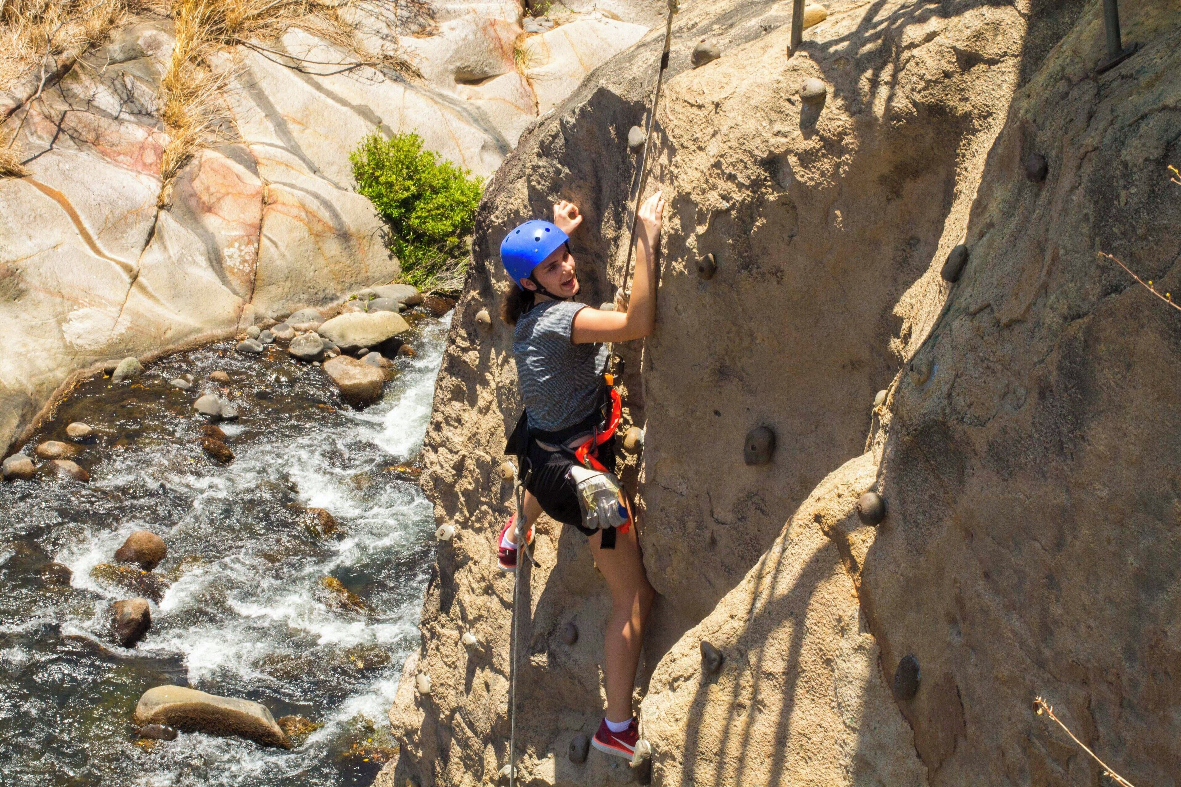 A person rock climbing on a rocky cliff with a river below.
