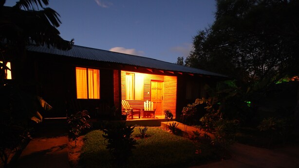 Een houten hut met een veranda, omringd door groen.