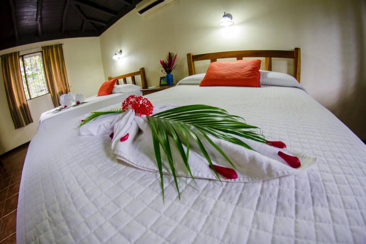 Un lit bien fait, recouvert d’une couette blanche, avec un oreiller rouge et une composition décorative de fleurs et de feuilles.