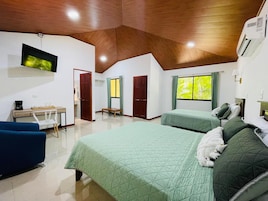 Quarto com duas camas, uma escrivaninha, uma cadeira, uma televisão e uma janela com cortinas.