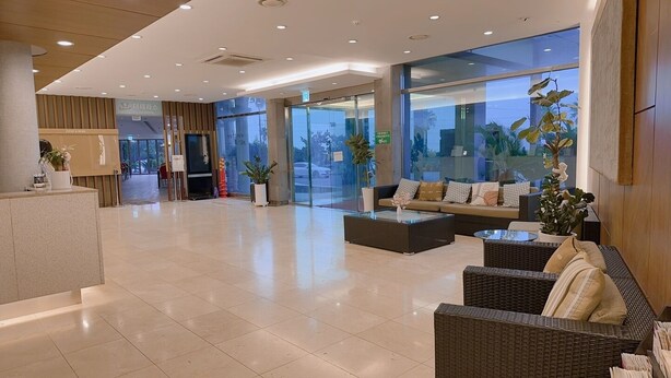 A spacious lobby with a reception desk, seating area, and large windows offering a view of the outdoors.