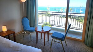 A hotel room with a bed, two chairs, a small table, and a view of the ocean through large windows.
