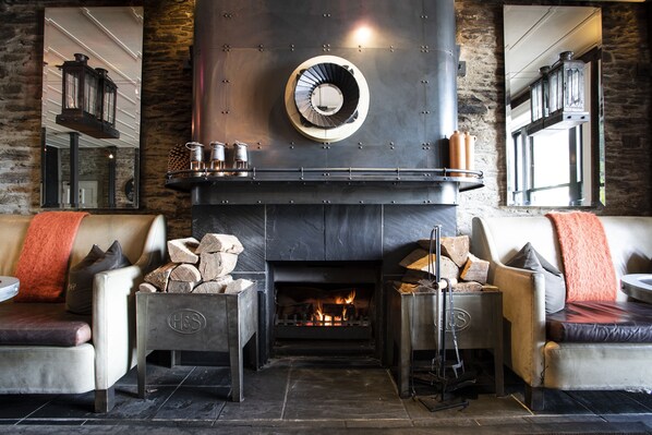 A cozy fireplace area with two sofas, a log fire, and a mirrored wall.