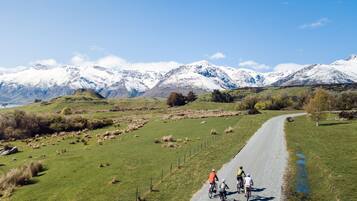 Een grindweg met fietsers, omgeven door groene velden en besneeuwde bergen op de achtergrond.