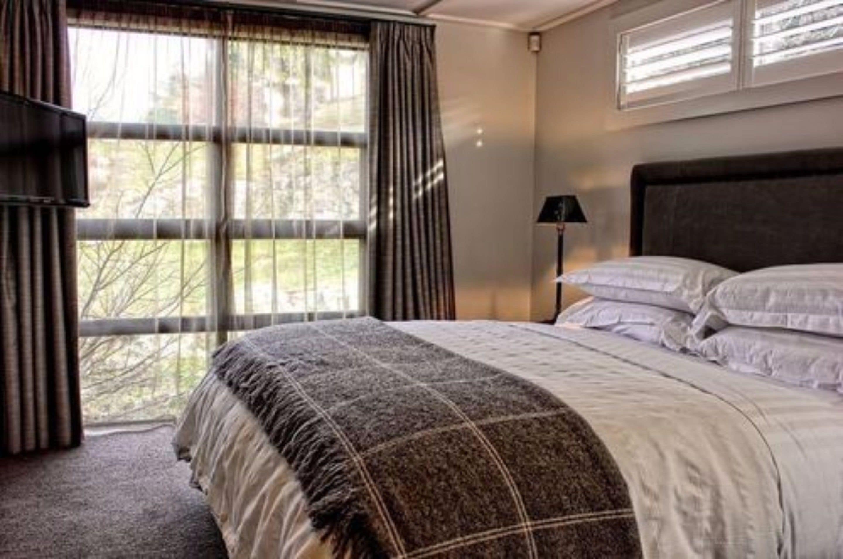 A hotel room with a large bed, a nightstand, a lamp, and a window with curtains.
