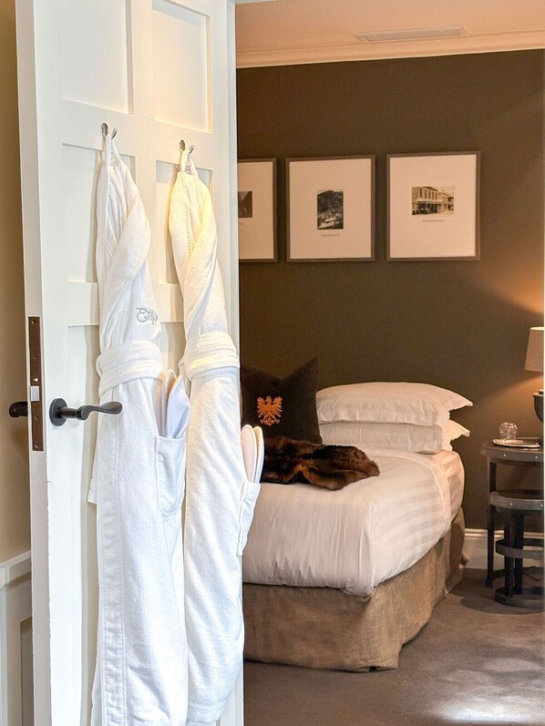 Un dormitorio con cama, mesita de noche, lámpara y un muro con cuadros.