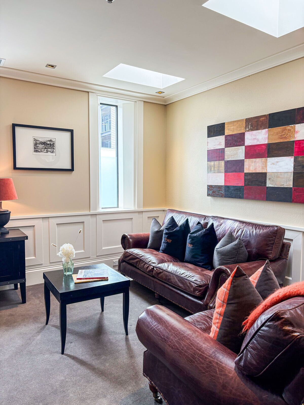 A living room with a leather sofa, a coffee table, a framed picture, and a colorful abstract painting.