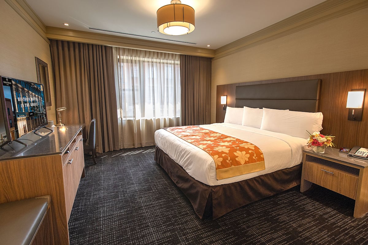 Une chambre d’hôtel avec un grand lit, un bureau avec un téléphone et un téléviseur situé à gauche.