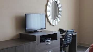 Habitación de hotel con televisión de pantalla plana, escritorio con silla, espejo y un cesto de basura.